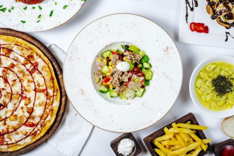 A colorful plaFGHFGHFGHte with salad, pizza, fries, and ravioli on a white table.